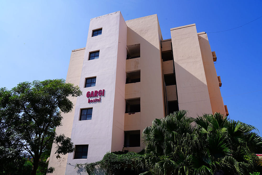 Gargi Hostel, with balconies, surrounding trees and plants, under a clear blue sky